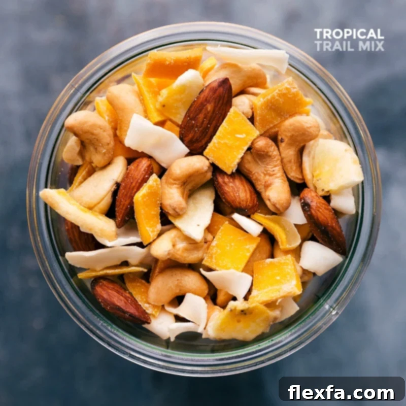 Delicious and healthy tropical trail mix full of nuts, dried fruits, and coconut, showcased in a clear glass jar.