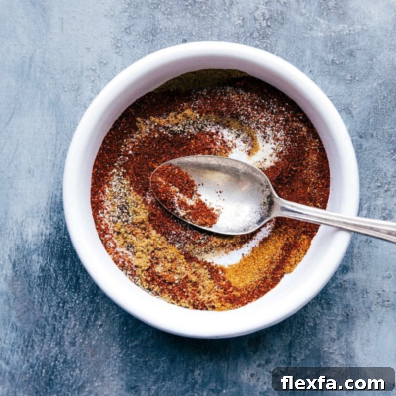 A bowl containing a vibrant seasoning mix, including chili powder, ground cumin, cayenne pepper, onion powder, garlic powder, salt, and pepper, prepared for the Quinoa Chili recipe.