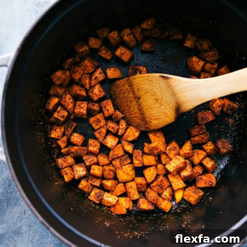 Sweet potatoes and spices are sautéing together in a pan, filling the kitchen with an aromatic and inviting fragrance, setting the foundation for the delicious Quinoa Chili.