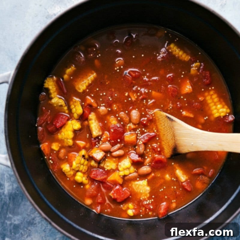 A large pot where all the ingredients for Quinoa Chili – sweet potatoes, quinoa, beans, corn, and tomatoes – are gently simmering, blending their flavors into a rich and comforting stew.