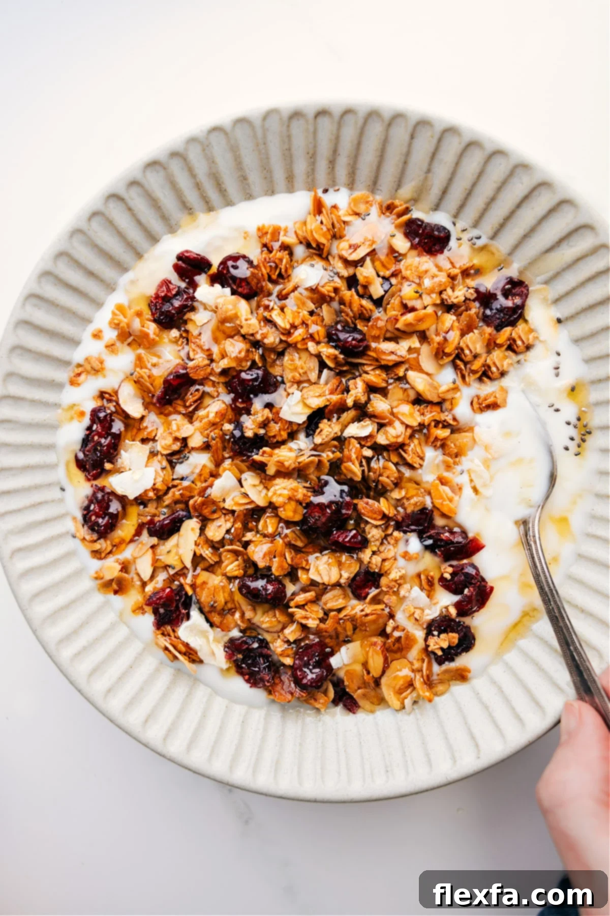 Honey Almond Granola sprinkled generously over creamy Greek yogurt, with a delicate drizzle of golden honey cascading over the top, garnished with fresh blueberries and a mint leaf.