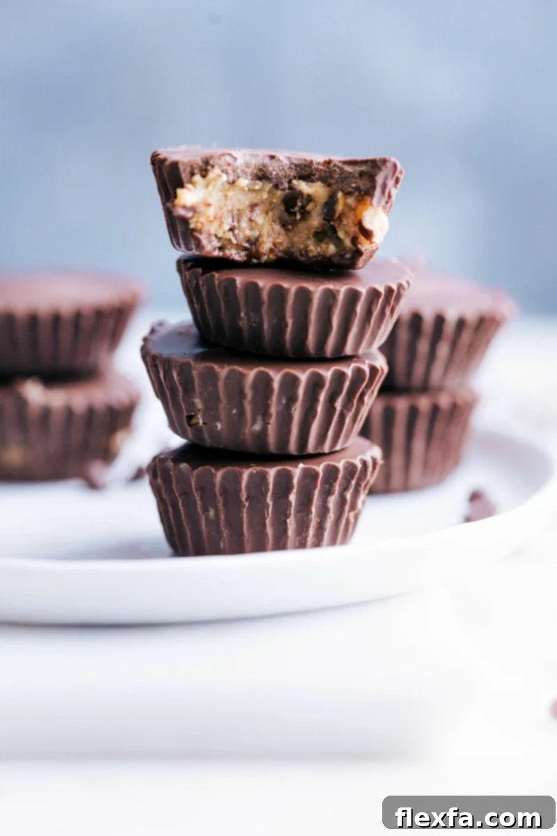 Photo of several Healthy Cookie Dough Cups stacked on a plate, showcasing their dark chocolate coating and cookie dough filling.