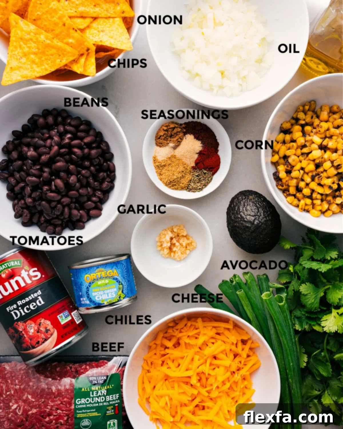 All the necessary ingredients for the easy taco skillet recipe are laid out, including a variety of seasonings, ground meat, fresh and frozen corn, creamy avocado, aromatic garlic, juicy tomatoes, mild green chiles, shredded cheese, crunchy tortilla chips, and vibrant fresh herbs, ready for quick assembly.