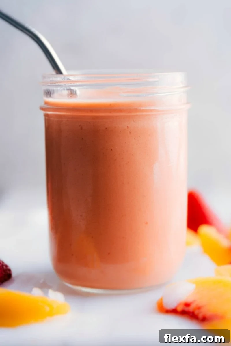 Close-up shot of a thick and creamy peach smoothie in a tall glass with a wide straw, garnished with fresh fruit, emphasizing its appealing texture.