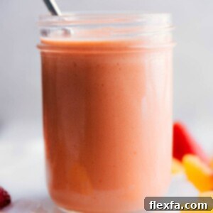 A vibrant peach smoothie in a glass with a straw, garnished with fresh peach slices and mint.