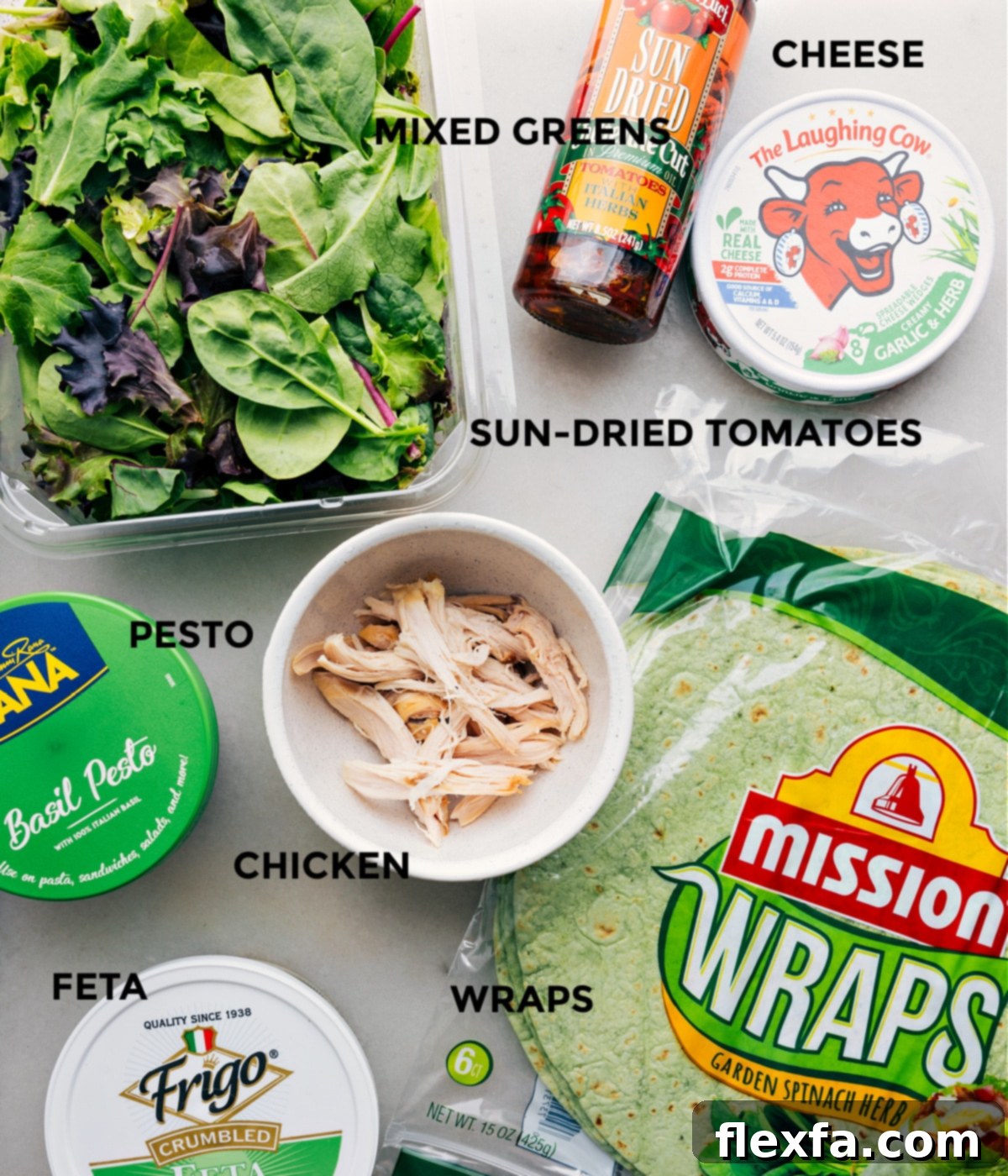All the ingredients for Mediterranean Wraps prepped out for easy assembly, including pesto, chicken, mixed greens, cheese, tortillas, and feta.