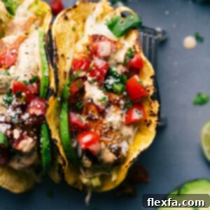 Two vibrant fish tacos filled with crispy slaw, seasoned fish, fresh pico, and a generous drizzle of cilantro-lime sauce.