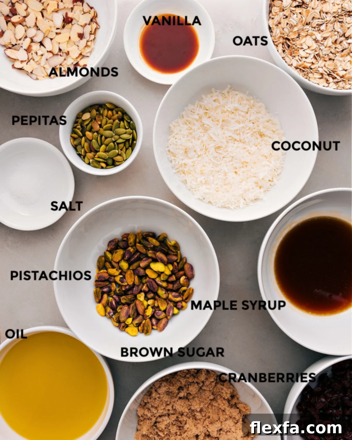 All the ingredients in this recipe are prepped for easy assembly: coconut, oats, vanilla, almonds, pepitas, maple syrup, pistachios, salt, brown sugar, cranberries, and oil.