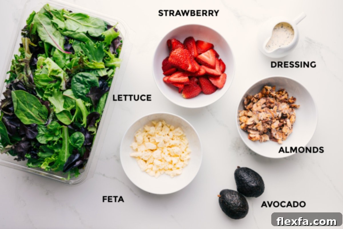 Ingredients for Strawberry Poppyseed Salad prepped and arranged, including fresh fruit, dressing, almonds, avocado, feta, and lettuce.