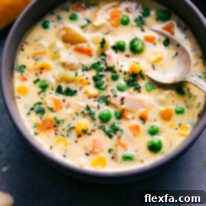 A close-up shot of a bowl of creamy Chicken Pot Pie Soup with a flaky puff pastry on the side, garnished with fresh parsley.