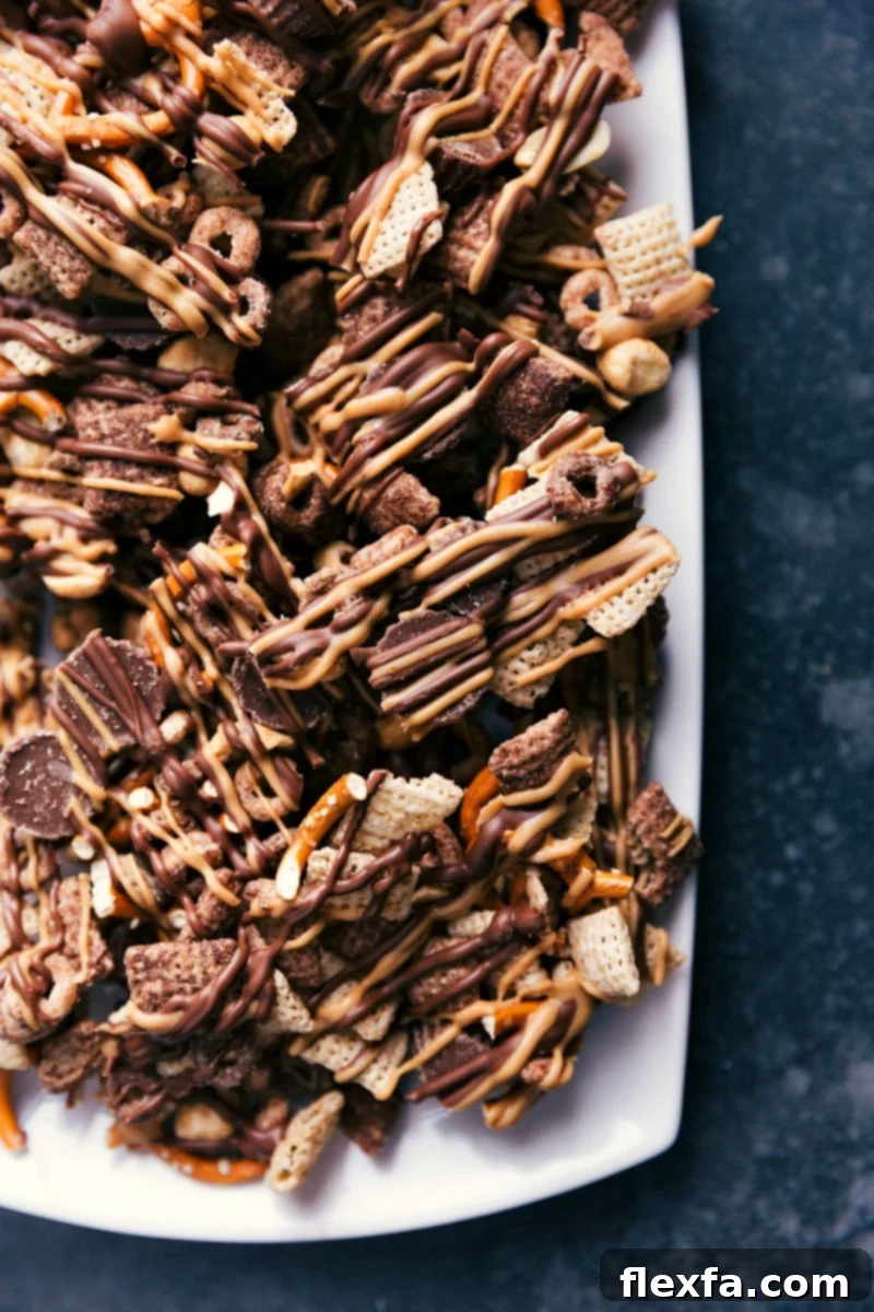 Flavorful Crunch - Chocolate-Peanut Butter Snack Mix Ready to Enjoy A large bowl overflowing with homemade Chocolate Peanut Butter Snack Mix, showcasing crunchy cereals, pretzels, peanuts, and mini peanut butter cups generously coated with melted chocolate and peanut butter drizzle. It's ready to be enjoyed, promising a perfect blend of sweet and salty flavors and a satisfying crunch.