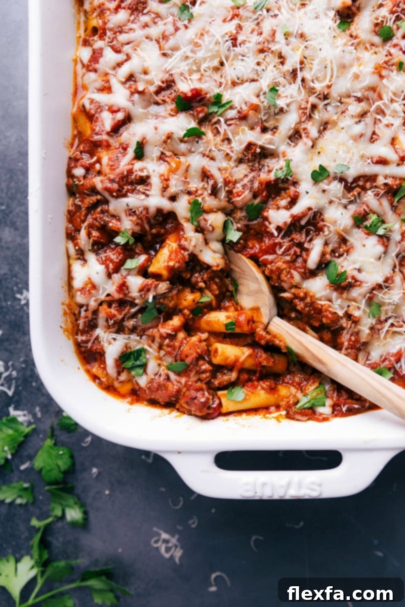 Finished baked ziti in a casserole dish, with a scoop taken out to reveal the warm, flavor-packed layers inside.