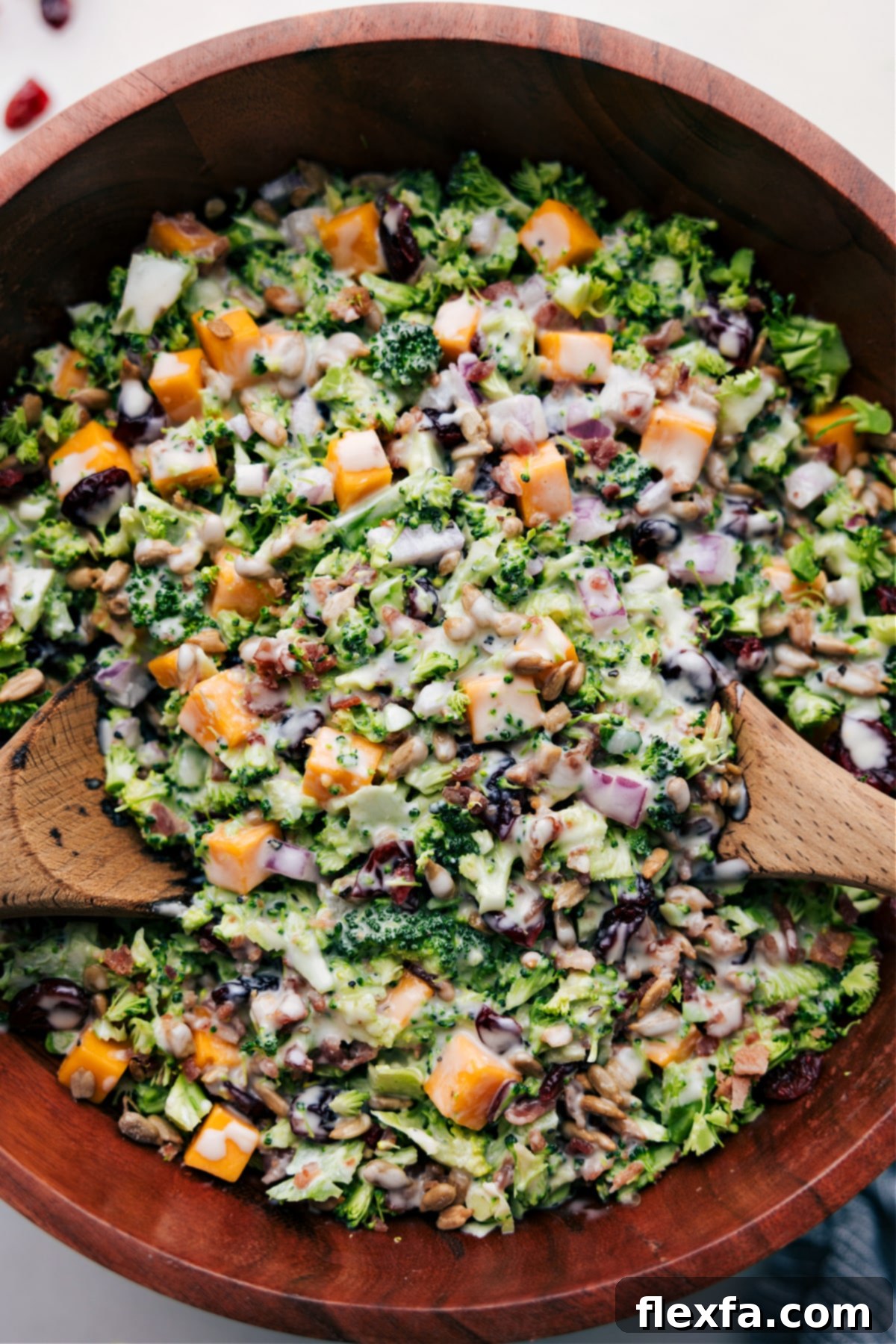 The Best Creamy Broccoli Salad Recipe for Potlucks A large bowl of creamy broccoli salad, featuring bright green broccoli florets, golden cheese cubes, red cranberries, and sunflower seeds, ready to be served.