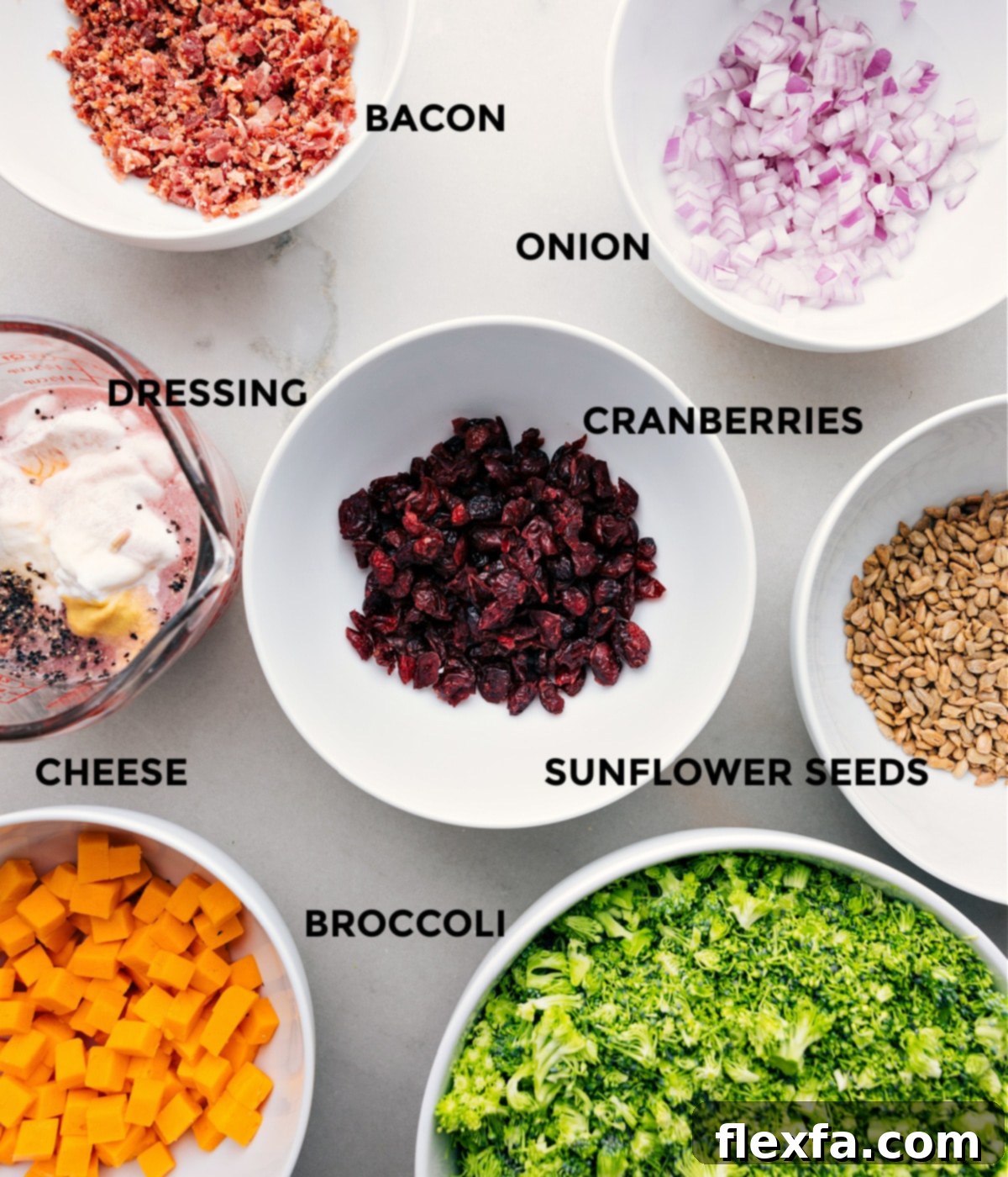 Essential Ingredients for Easy Broccoli Salad All fresh ingredients for broccoli salad prepped and laid out on a wooden board, including chopped broccoli, cubed cheese, dried cranberries, bacon crumbles, sunflower seeds, and sliced red onion, ready for assembly.