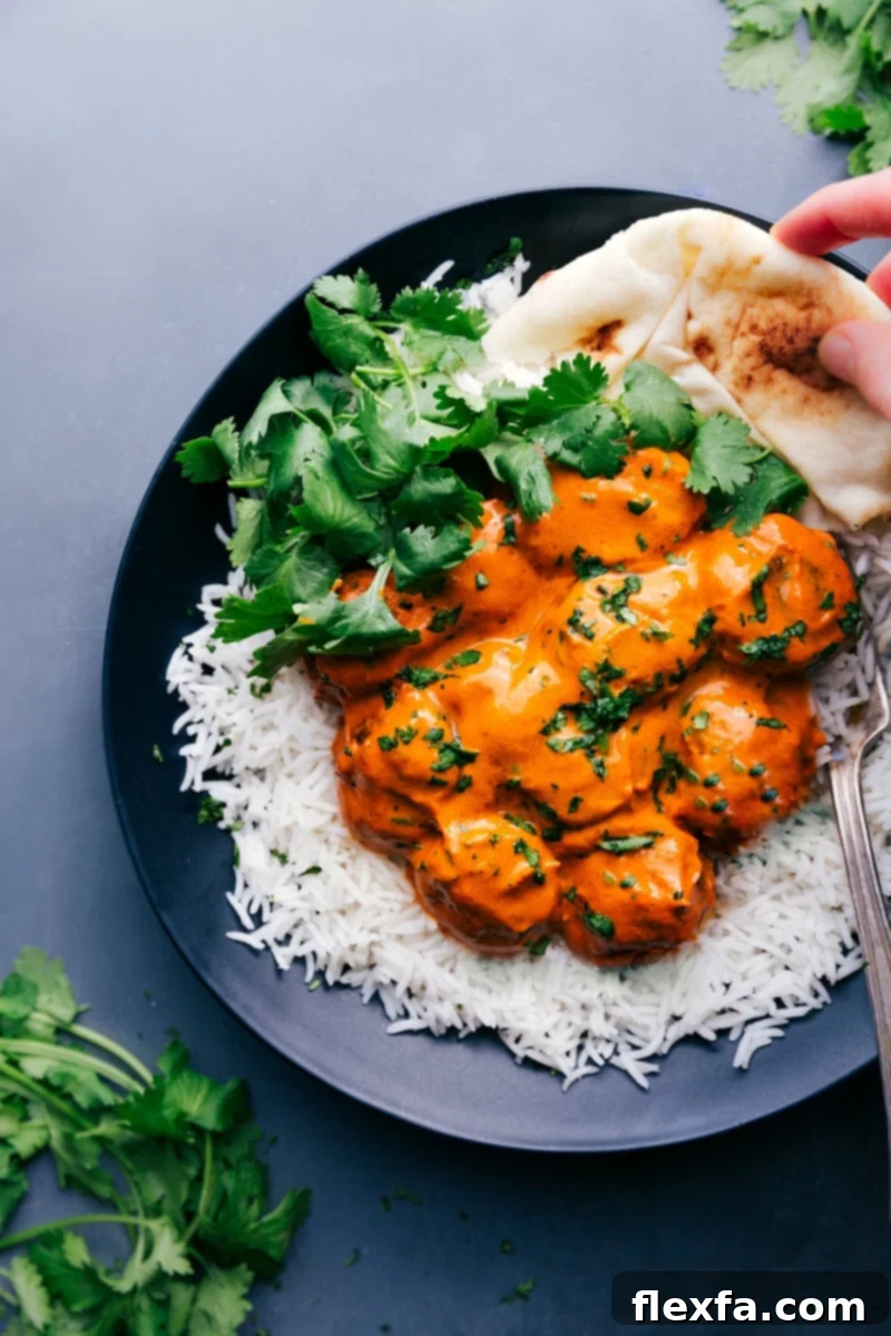 Plate with butter chicken meatballs served on a bed of rice, garnished with fresh cilantro, with naan bread on the side. A complete, delicious meal.
