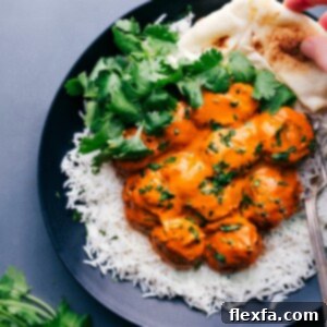 Plate with butter chicken meatballs served on a bed of rice, garnished with fresh cilantro, with naan bread on the side.