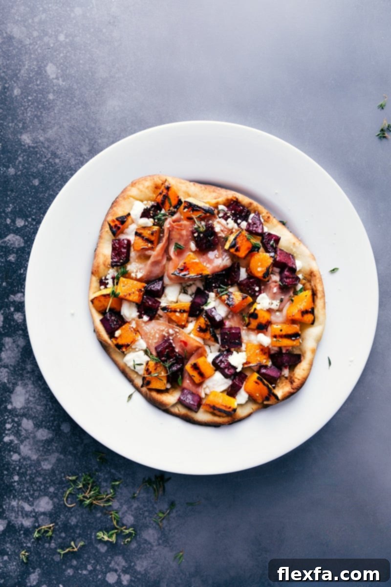 Overhead view of freshly grilled beet and goat cheese flatbread, adorned with colorful beets, golden butternut squash, prosciutto, and fresh thyme