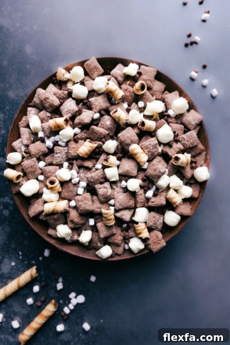 A large bowl brimming with homemade Hot Chocolate Snack Mix, showcasing crunchy chocolate Chex, fluffy white chocolate-coated marshmallows, and scattered chocolate chips.