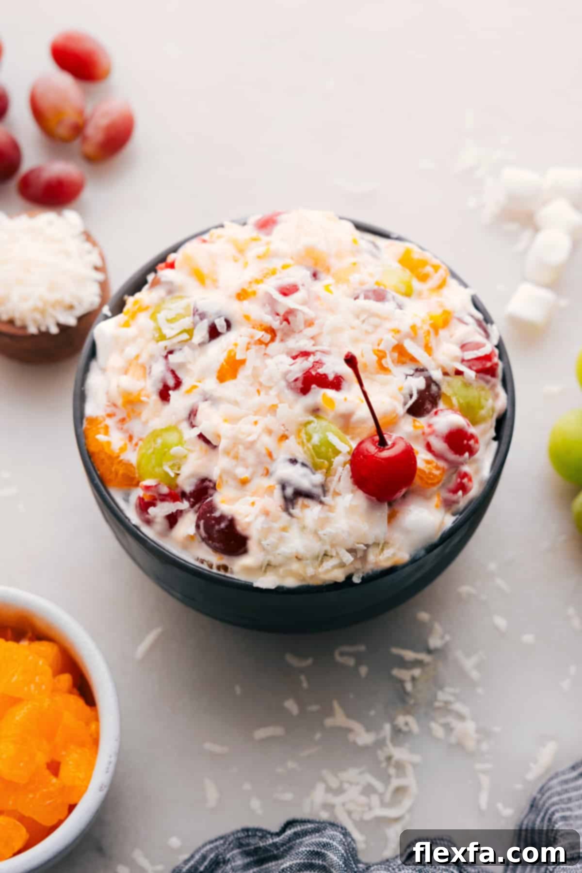 A vibrant Ambrosia Salad in a large glass bowl, garnished with a bright red maraschino cherry on top, ready to be served.