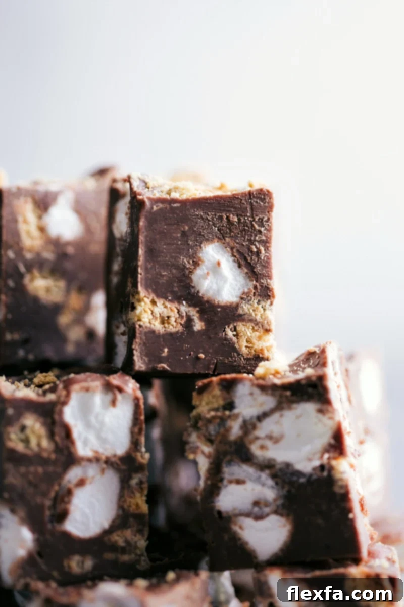 Easy Stovetop S'mores Fudge: A perfect blend of milk chocolate, graham crackers, and marshmallows for a delightful no-bake dessert. Several pieces of rich, gooey S'mores Fudge on parchment paper, showcasing the chocolate, graham crackers, and marshmallows.