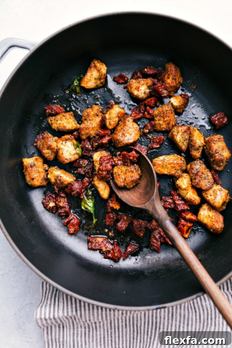 Process shot showing chicken pieces and chopped sun-dried tomatoes being sautéed together in a large nonstick pot.