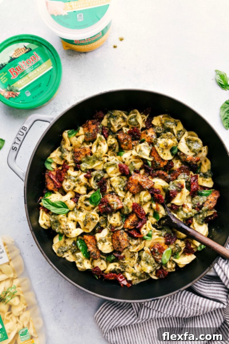 Overhead image of the finished Pesto Chicken Tortellini in the cooking pan, garnished with fresh basil and Parmesan, ready to be served.