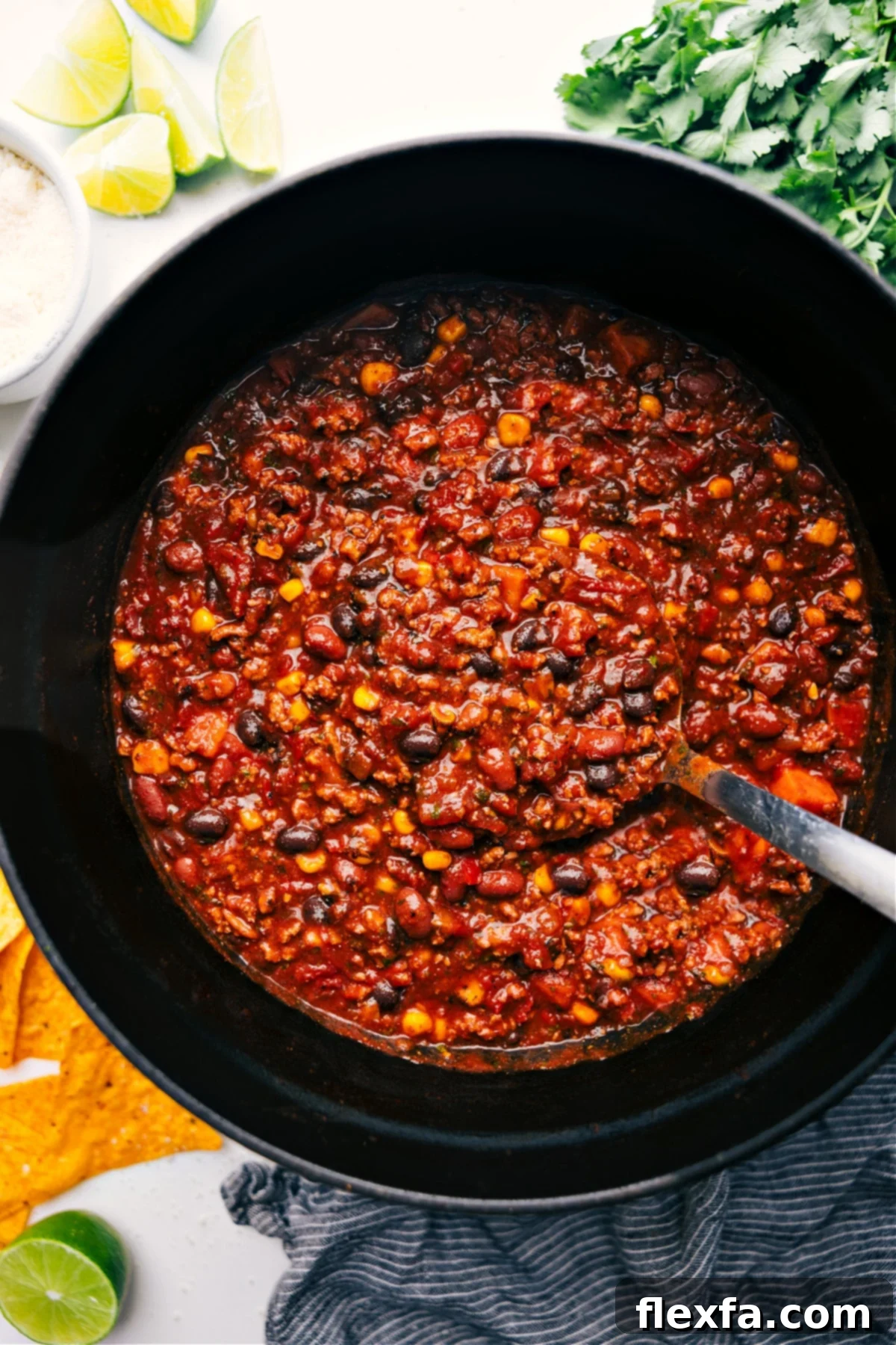 A large, steaming pot filled with rich, savory Turkey Chili, with a ladle poised to serve a hearty portion. The chili is garnished with fresh cilantro and a dollop of sour cream.