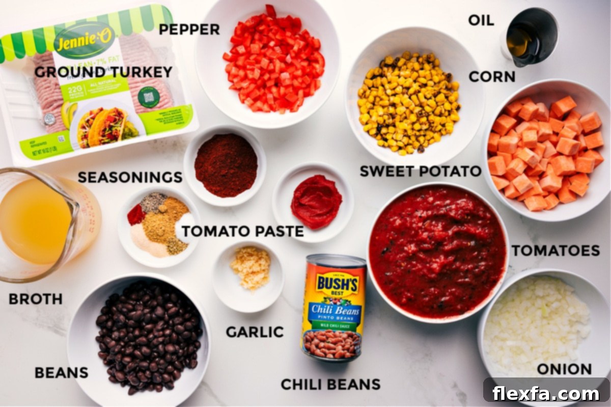 An organized display of all the essential ingredients for Turkey Chili, including raw ground turkey, various beans, spices, garlic, tomato paste, bell peppers, sweet potatoes, canned tomatoes, onion, corn, and olive oil, all prepped and ready for cooking.