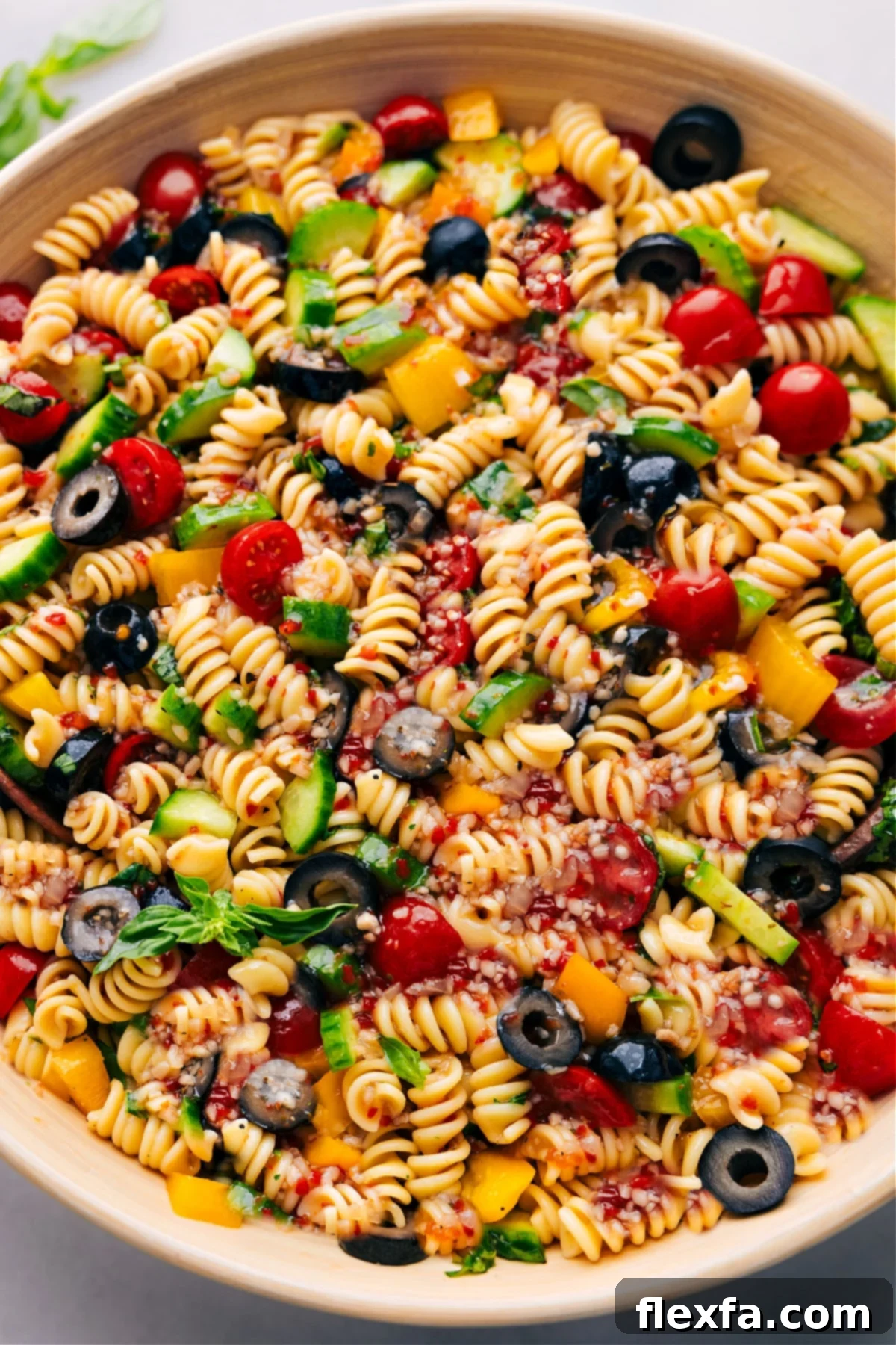 A vibrant bowl of pasta salad, generously mixed with colorful vegetables and a zesty dressing, ready to be served and enjoyed.