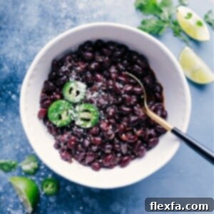 A perfectly cooked bowl of homemade black beans, garnished with fresh cilantro and a lime wedge, highlighting its rich texture and appetizing appearance.