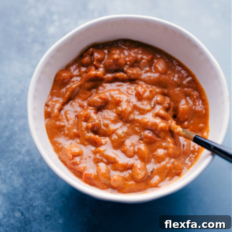Close-up shot of saucy pinto beans in a bowl with a serving spoon, showcasing their creamy texture.