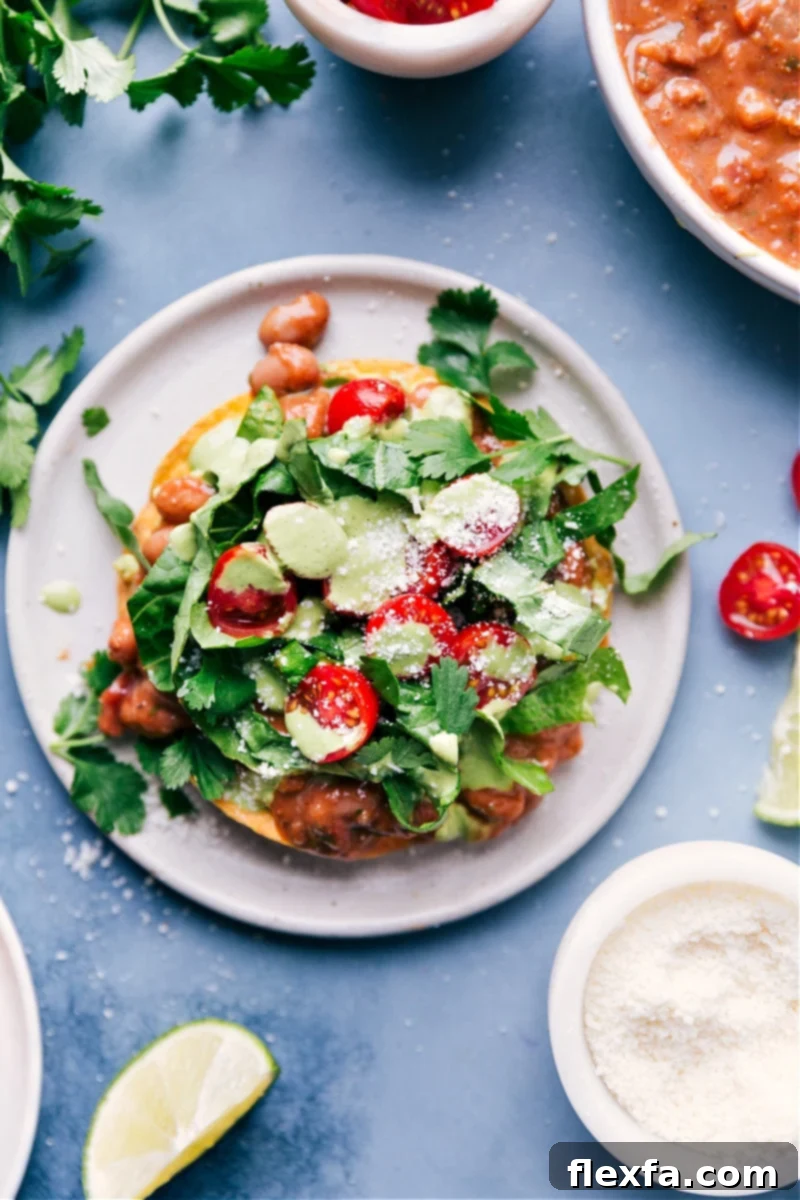 Crispy Bean Tostadas: Smashed avocado, spiced pinto beans, fresh veggies, and a quick cilantro-lime sauce. Overhead image of crispy Bean Tostadas topped with avocado, beans, lettuce, tomatoes, and cilantro-cashew sauce.