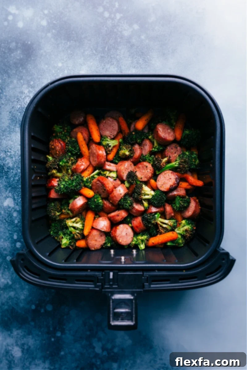 Delicious air-fried chicken sausage, carrots, and broccoli tossed with herbs, served on a bed of quinoa and mixed greens with a quick honey mustard sauce. This nutritious, filling meal is ready in under 30 minutes! Overhead view of the sausage, carrots, and broccoli beautifully cooked in an air fryer basket, ready to be served.