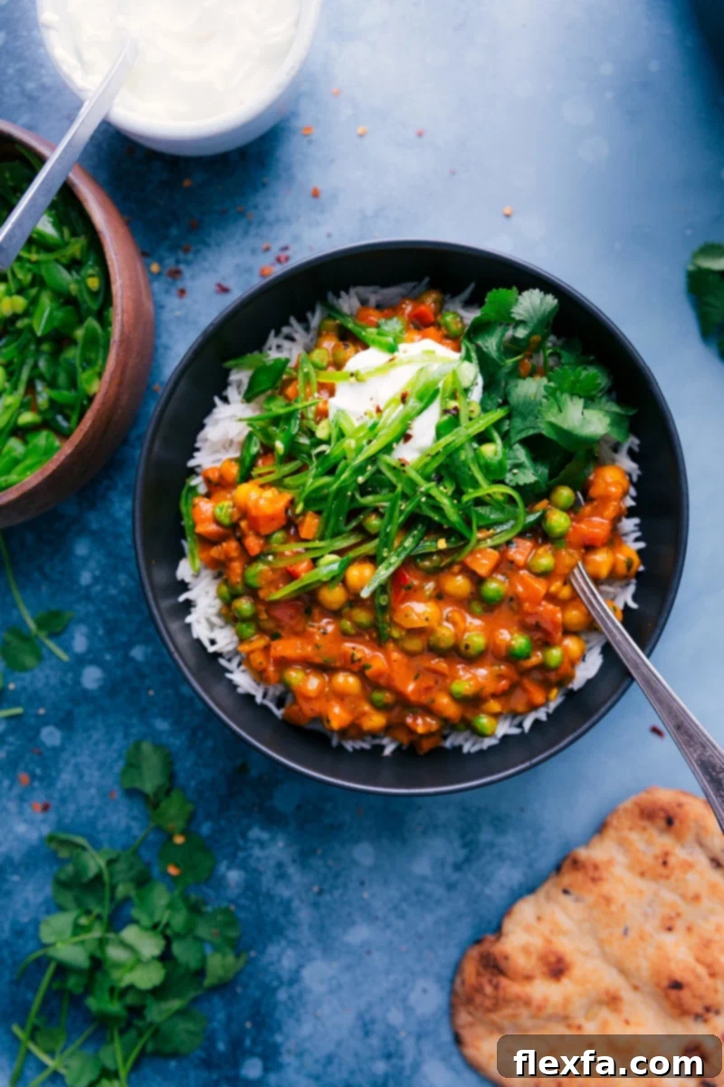 A vibrant bowl of Vegetarian Tikka Masala, garnished with fresh snap peas, a swirl of Greek yogurt, and fragrant cilantro, ready to be served.