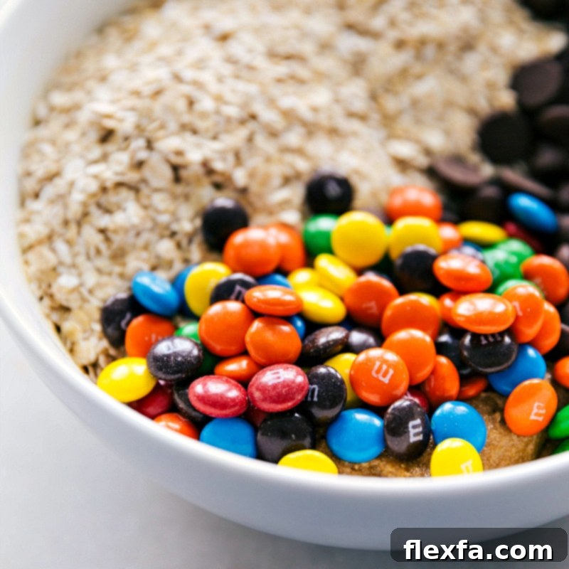 Quick oats, assorted chocolate chips, and colorful M&M's being gently stirred into a bowl of gluten-free cookie dough.