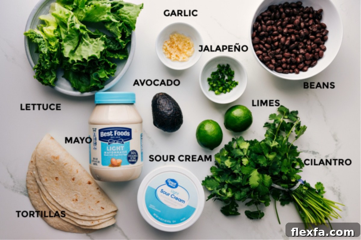 All the fresh ingredients for Black Bean Wraps beautifully laid out: crisp green lettuce, ripe avocados, juicy limes, a can of black beans, creamy sour cream, rich mayonnaise, and fragrant fresh cilantro, alongside soft tortillas.