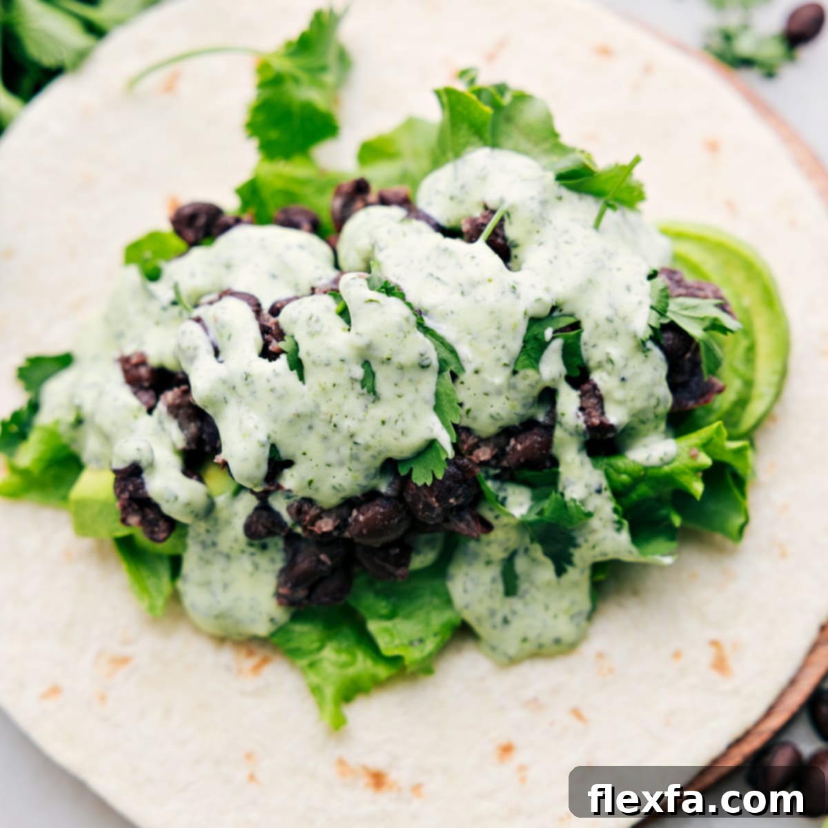 An appetizing Black Bean Wrap sliced in half, showcasing its vibrant layers: fresh green lettuce, perfectly seasoned black beans, creamy avocado slices, and a rich drizzle of the signature cilantro-lime sauce, ready for enjoyment.