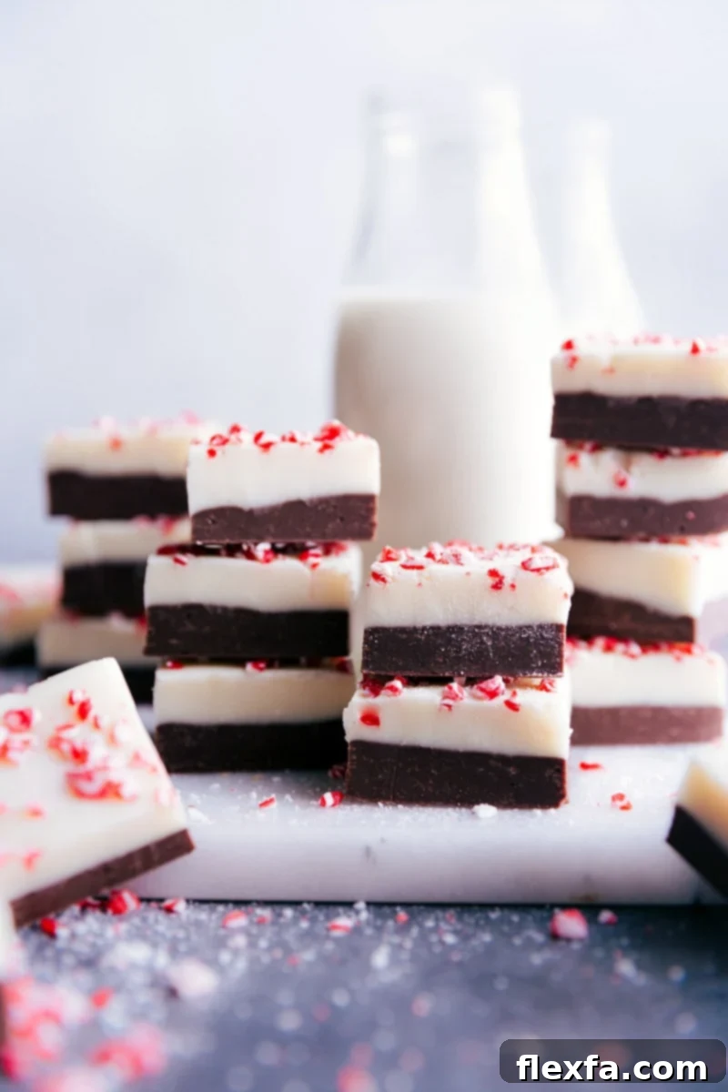 Stacked squares of rich Peppermint Fudge, showcasing its beautiful layers and festive peppermint crunch topping.