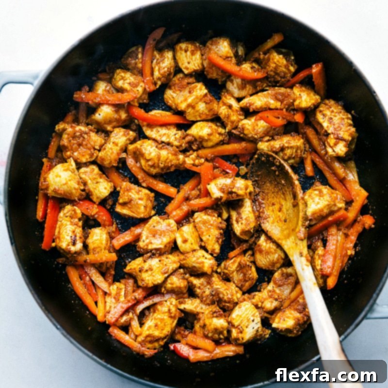 Chicken breast pieces and sliced red bell peppers cooking in a large pan, beginning to brown and release their flavors, ready for the curry base.