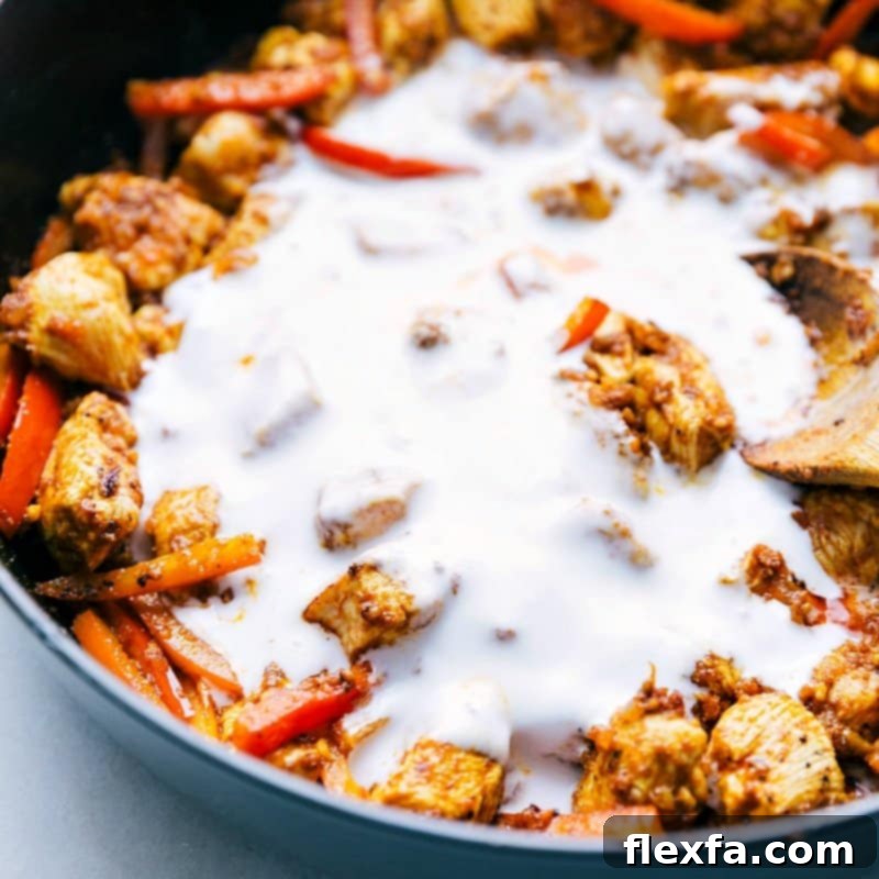 Creamy coconut milk being poured into a pan with sautéed chicken and red peppers, forming the rich, luscious sauce for the chicken curry.