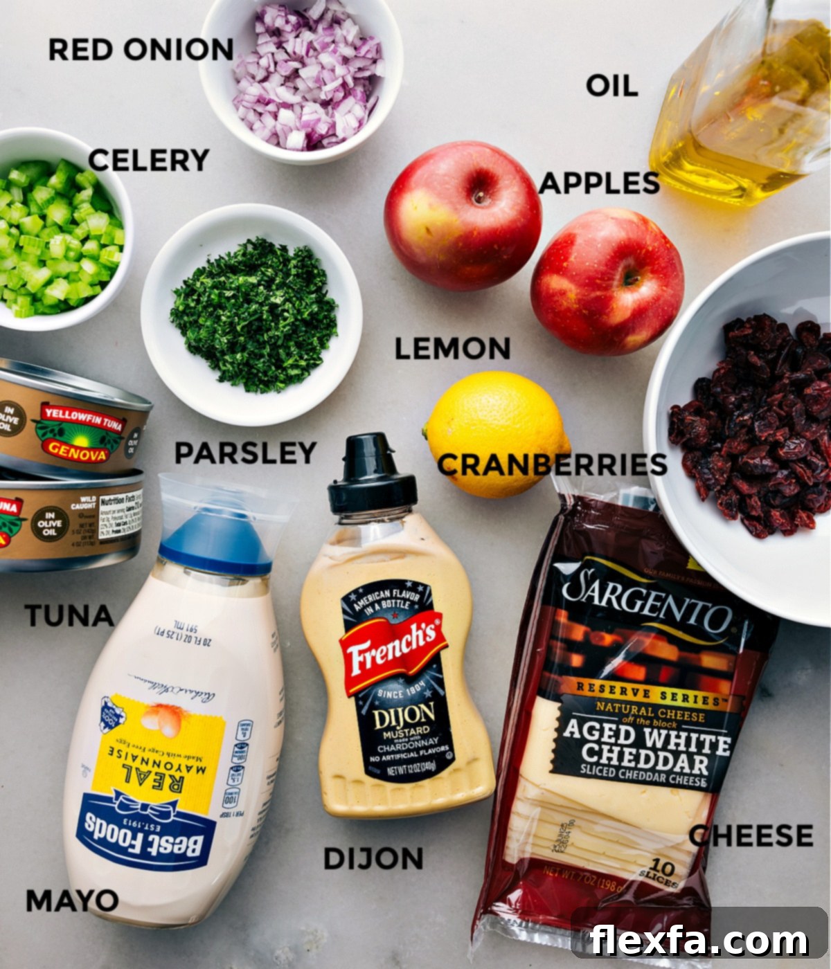 A vibrant display of all the fresh ingredients required for this easy tuna salad recipe, neatly prepped and arranged. Includes canned tuna, dried cranberries, crisp apples, fresh lemon, olive oil, red onion, celery, flat-leaf parsley, sharp cheddar cheese, Dijon mustard, and creamy mayonnaise.