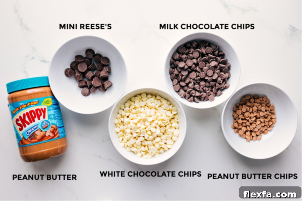 Ingredients prepped in small bowls for easy assembly: peanut butter, mini Reese’s cups, white chocolate chips, milk chocolate chips, and peanut butter chips.