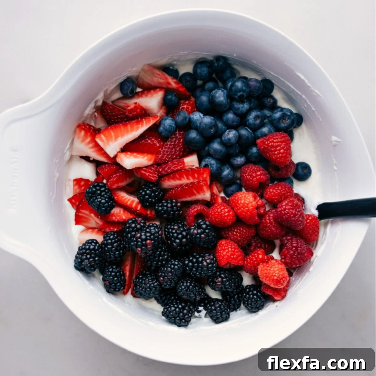 Berries being mixed into the creamy dressing for Cheesecake Fruit Salad.