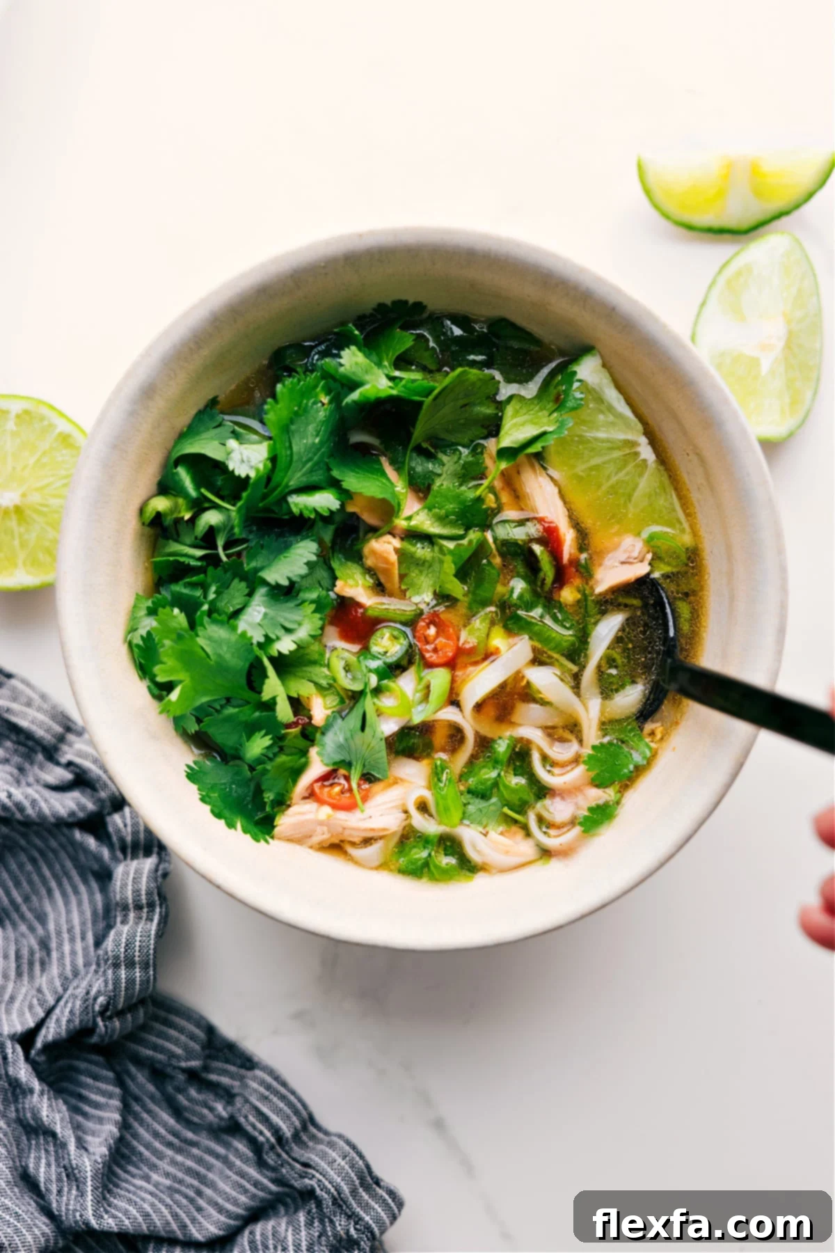 Chicken Pho Recipe in a bowl with fresh cilantro, lime, and peppers on top. Garnish with fresh herbs, lime wedges, and a dash of sriracha for an authentic touch.