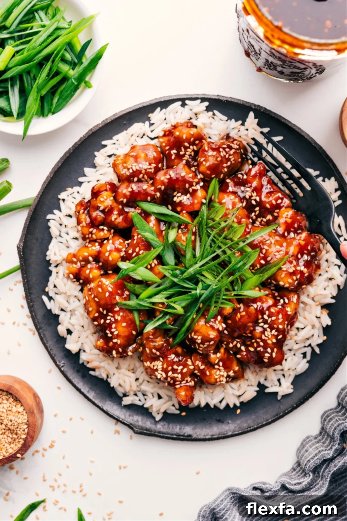 Korean Fried Chicken Delight 2 Korean Chicken Recipe on a bed of rice with fresh green onions and sesame seeds on top.