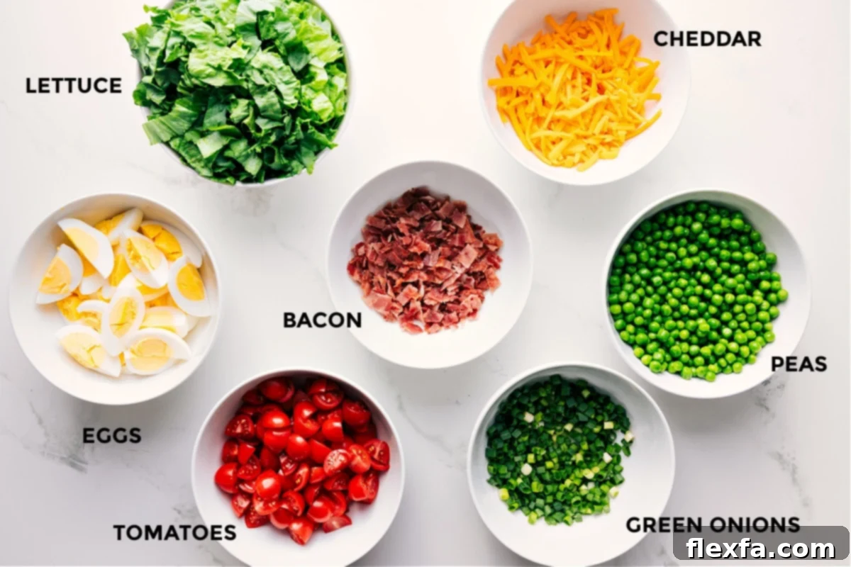 All the vibrant ingredients for the 7 Layer Salad meticulously prepped and arranged, including crisp lettuce, shelled peas, sliced green onions, quartered tomatoes, hard-boiled eggs, shredded cheddar cheese, and crumbled bacon, ready for assembly.