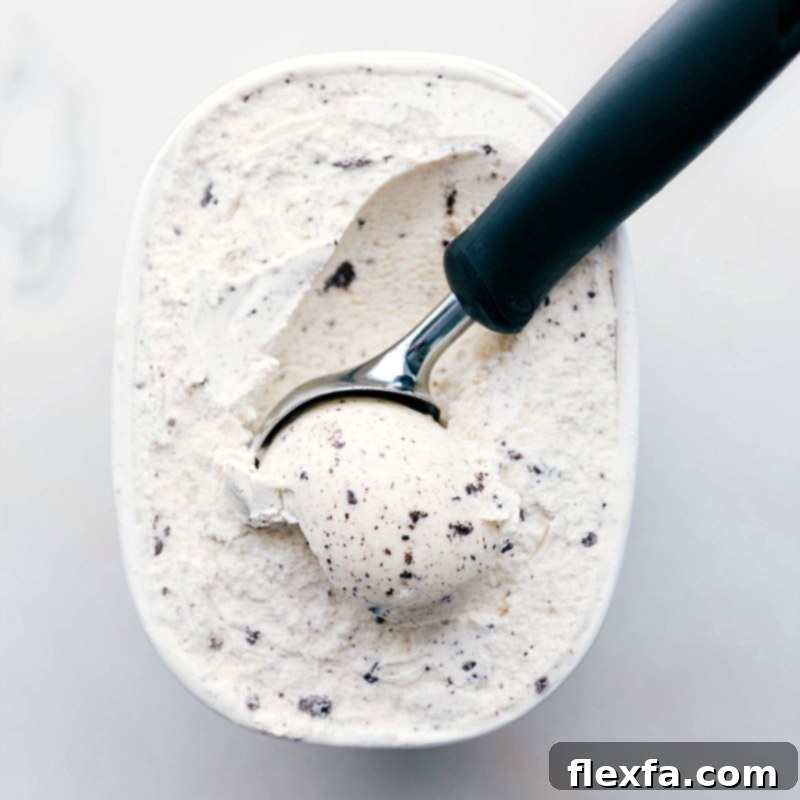 A large container of cookies and cream ice cream with a scoop resting in it, ready to be added to the cake layers.