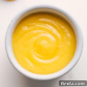 Close-up of vibrant, smooth homemade lemon curd in a glass jar, ready to be served.