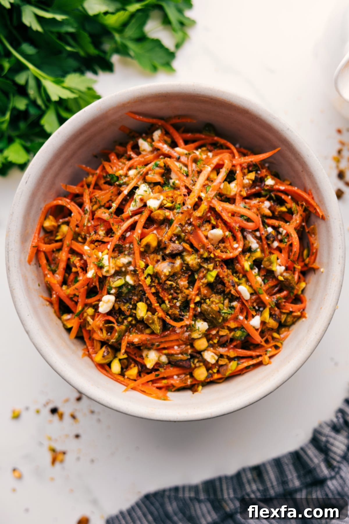A beautifully presented ribbon carrot salad in a rustic bowl, generously tossed with its zesty dressing and adorned with bright green pistachios and a sprinkle of fresh herbs.