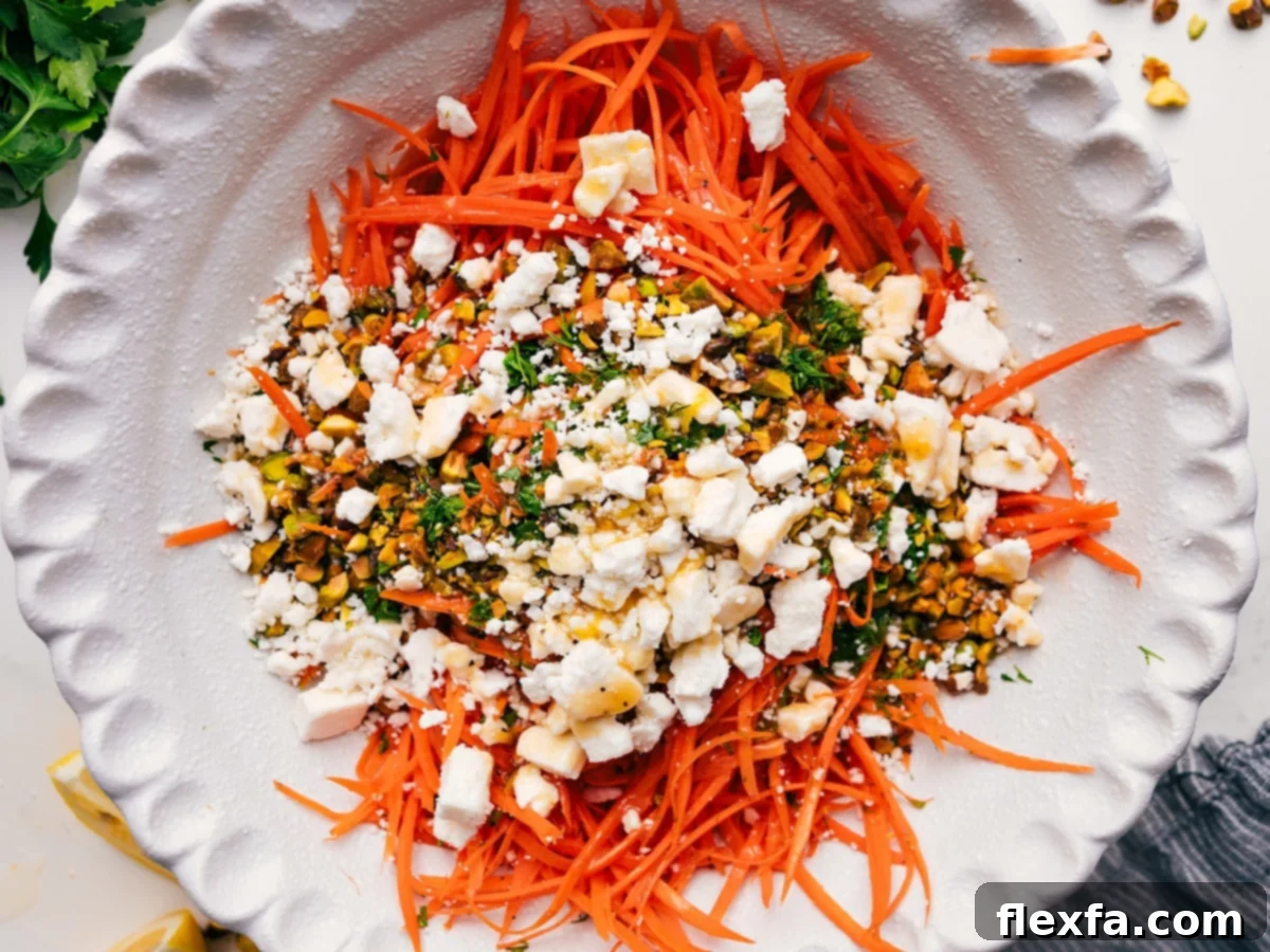 The vibrant components of the ribbon carrot salad, including julienned carrots, chopped pistachios, and fresh herbs, are gathered in a large mixing bowl, ready to be dressed and tossed together.